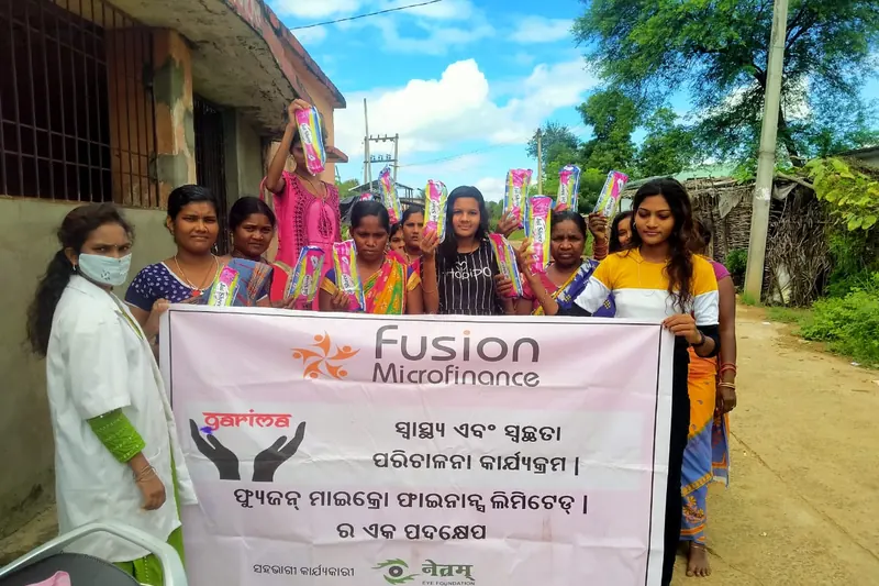 Women at a Project Garima awareness session in Kalahandi, holding sanitary napkin packs behind the programme banner