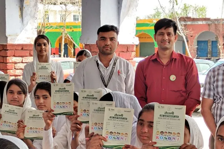 Smiling schoolgirls holding their Project Roshini screening cards